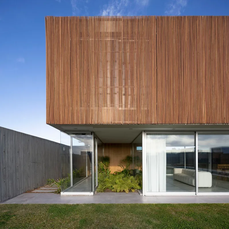 Cantilevered timber-clad volume above glass-walled ground floor with courtyard planting and lawn