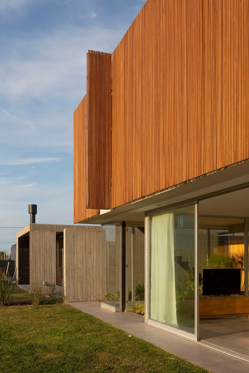 Vertical timber slat facade above glazed walls and grass lawn under a clear blue sky