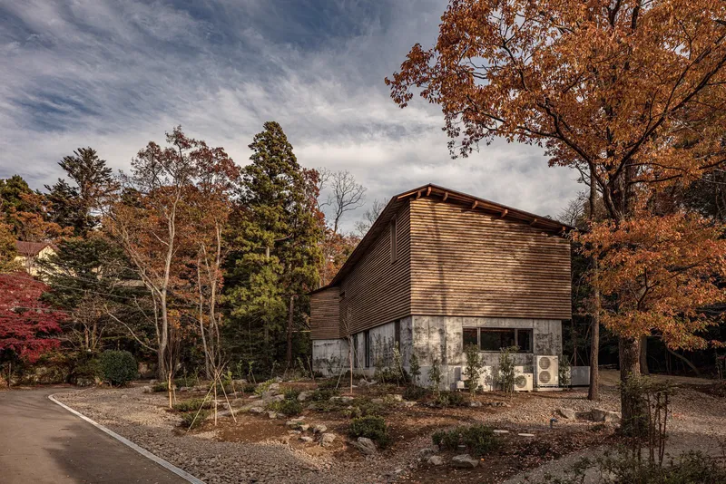 Corner view of the horizontal wood-slatted facade with HVAC units at ground level under autumn foliage
