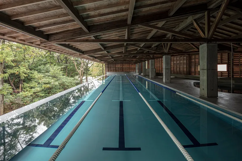 Indoor lap pool with lane markers beneath exposed timber roof trusses and concrete columns