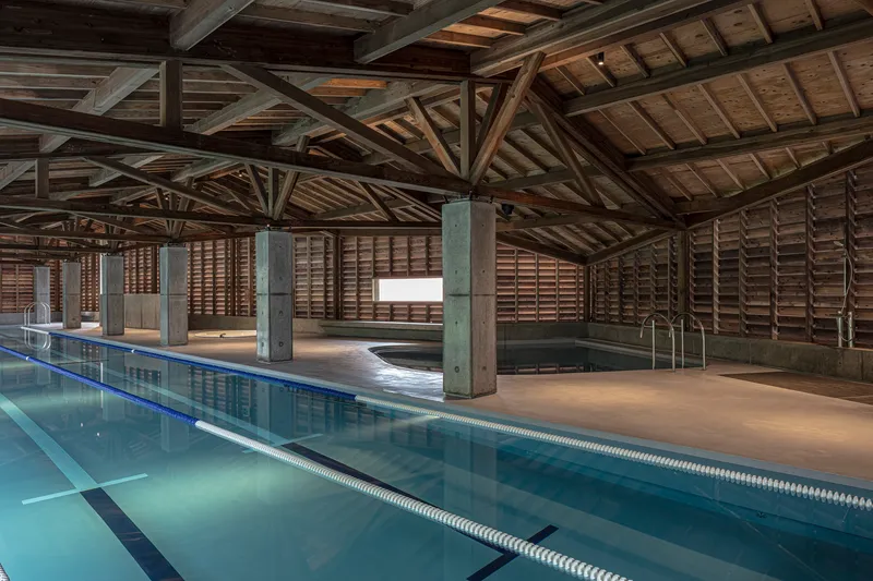Interior lap pool with exposed timber roof trusses and concrete columns in daylight
