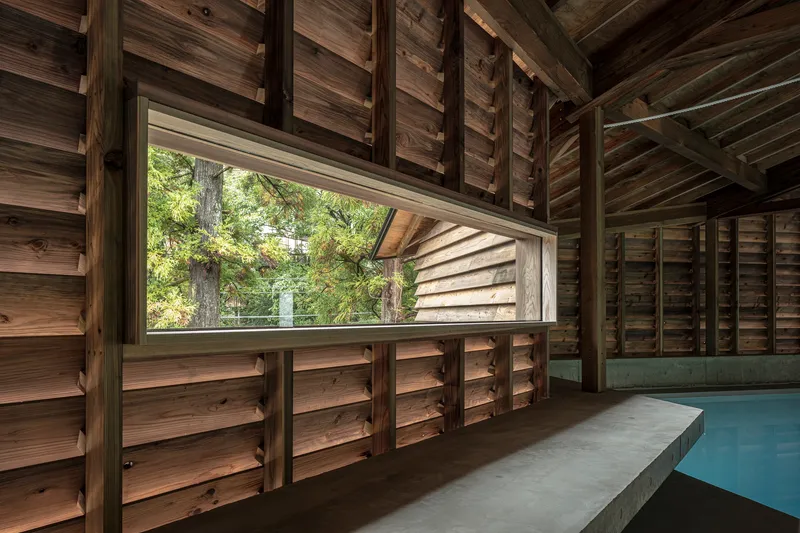 Horizontal window framing forest view within timber slatted wall beside the pool edge