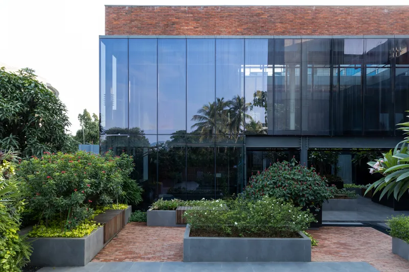 Rooftop courtyard with raised metal planters and glass-enclosed volumes reflecting surrounding palms