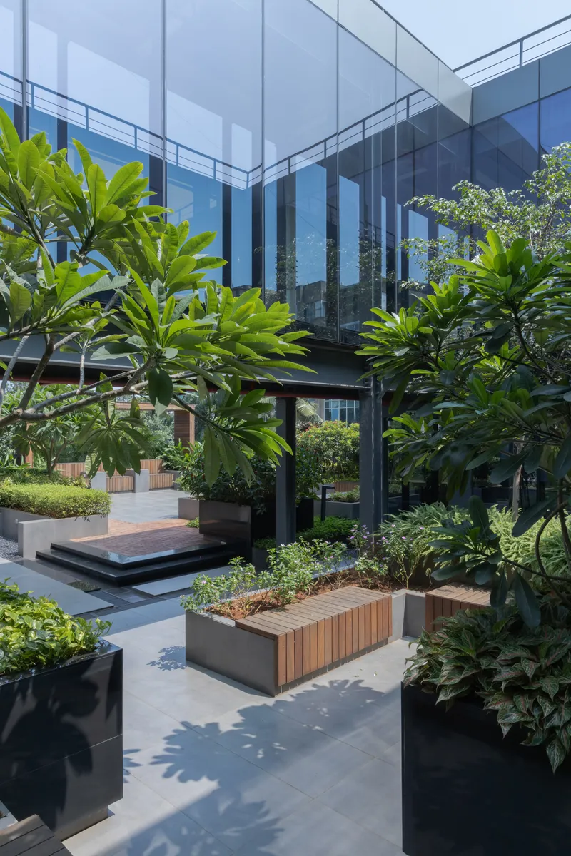 Landscaped courtyard with timber planters and black steel columns beneath the glass bridge