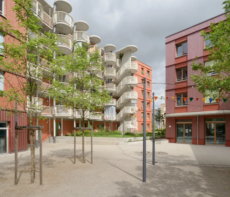 Central courtyard plaza with young trees and rows of cylindrical balcony towers under dark storm clouds