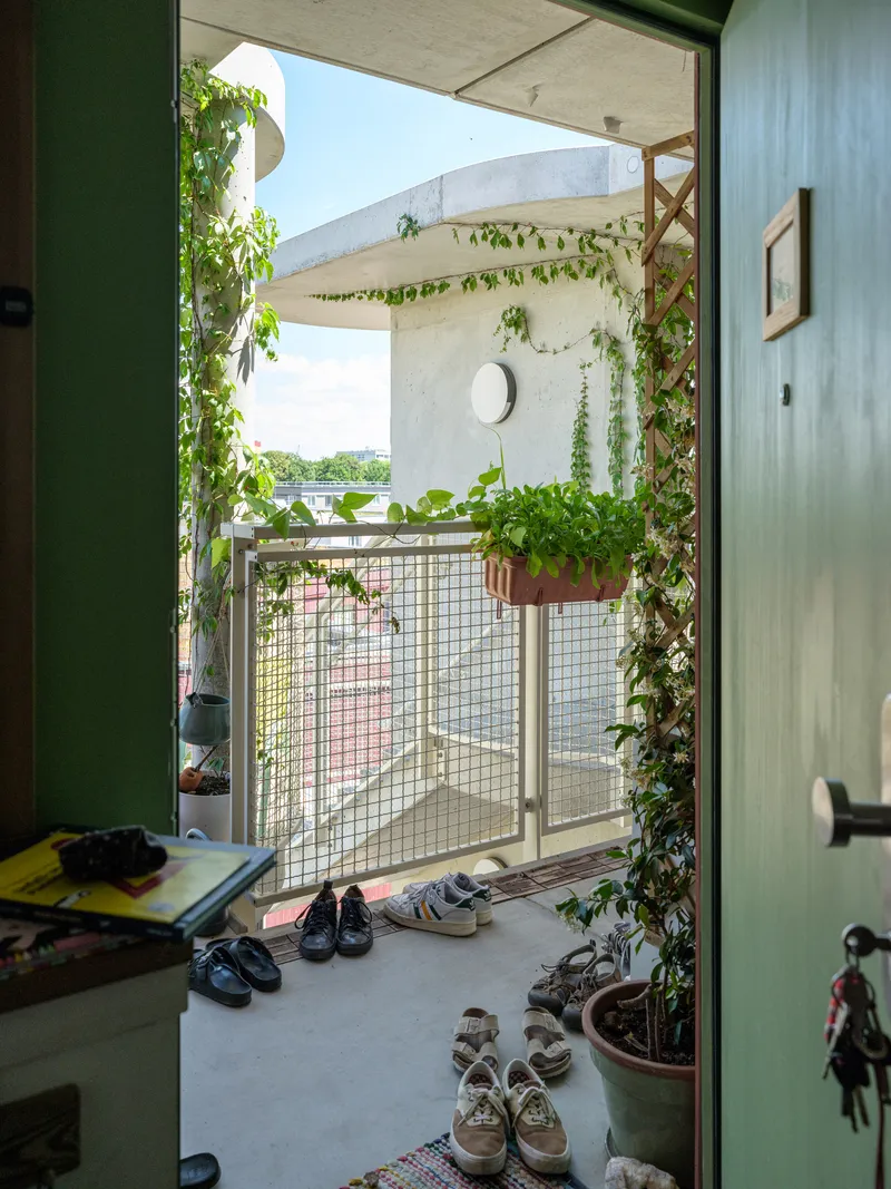 Balcony threshold with mesh railing, climbing vines, and rows of shoes on concrete floor
