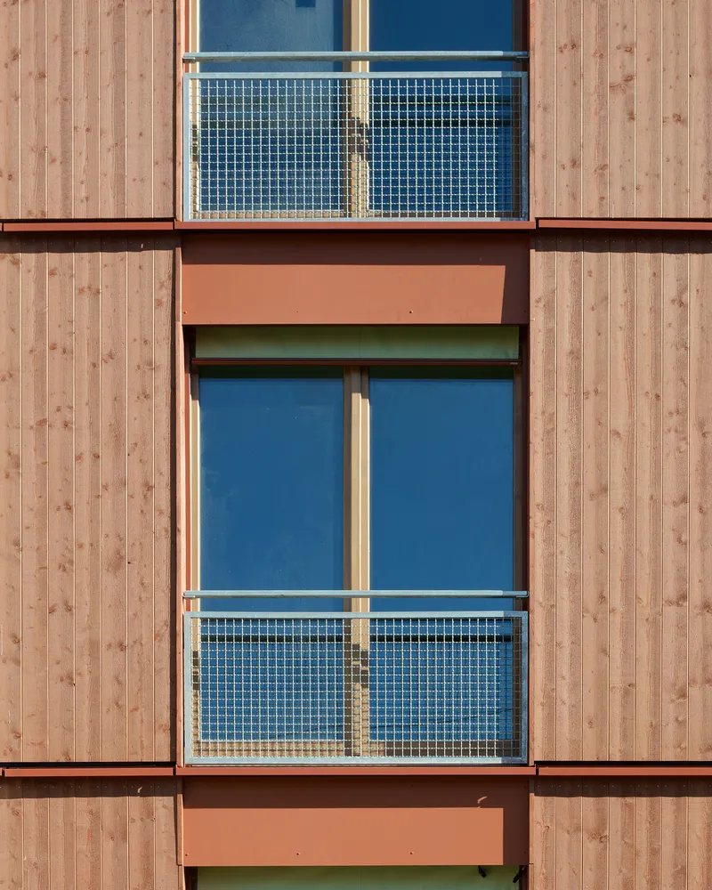 Facade detail showing stacked balconies with mesh railings framed by vertical timber cladding