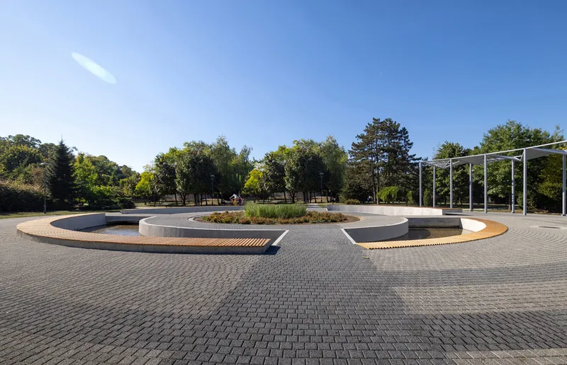 Three lobed water pools with central planted island surrounded by grey cobblestone paving and white canopy structures