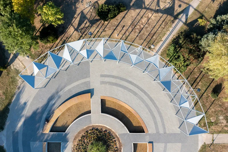 Aerial view of the circular amphitheater with blue-paneled canopy and concentric paving patterns in late afternoon light