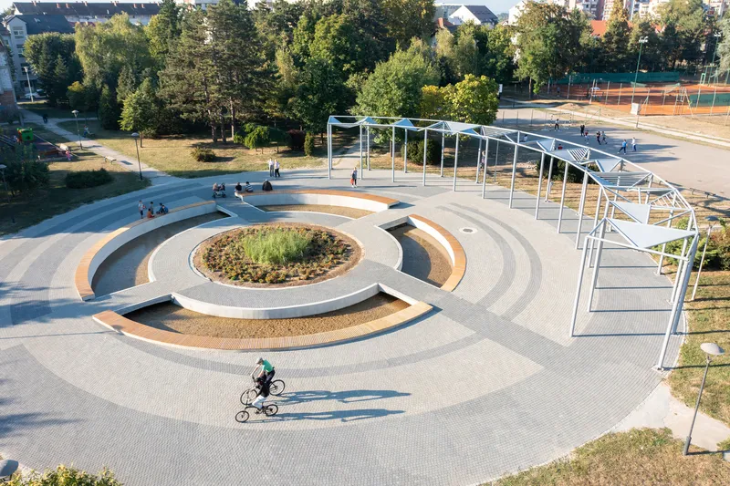 Overhead view of the circular plaza with concentric seating rings and a child cycling across the paved surface