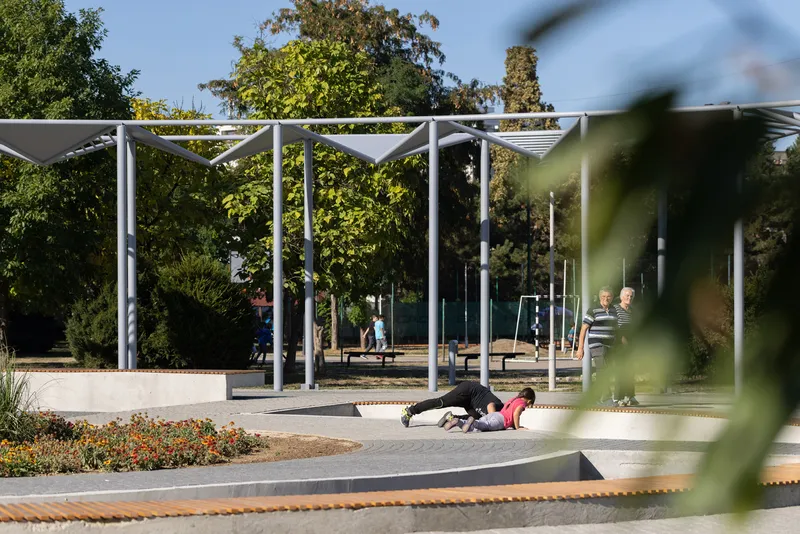 Children playing on the curved concrete seating platforms beneath the white steel canopy structure