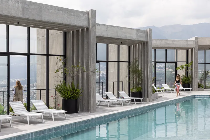 Rooftop pool deck with concrete columns, steel-framed glazing, and chaise lounges overlooking mountain ridges