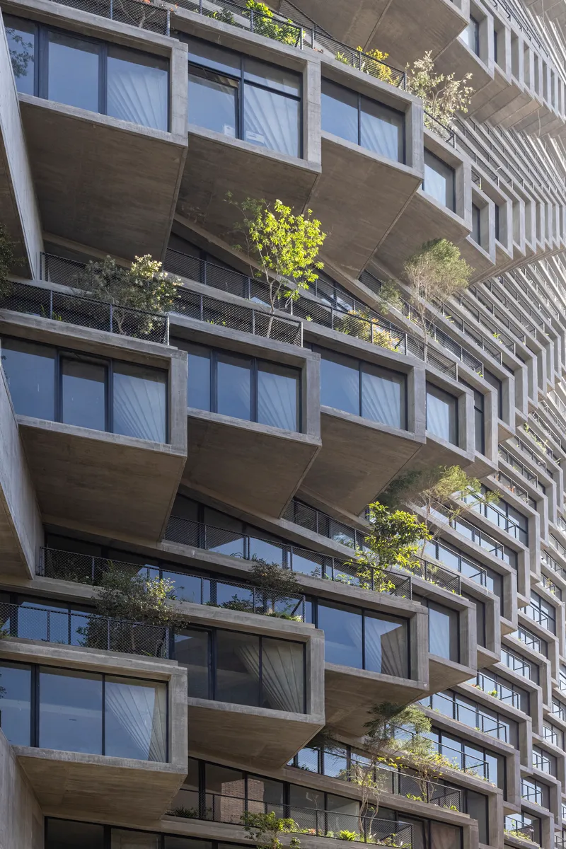 Stacked concrete balconies with planted trees and floor-to-ceiling glazing in bright daylight