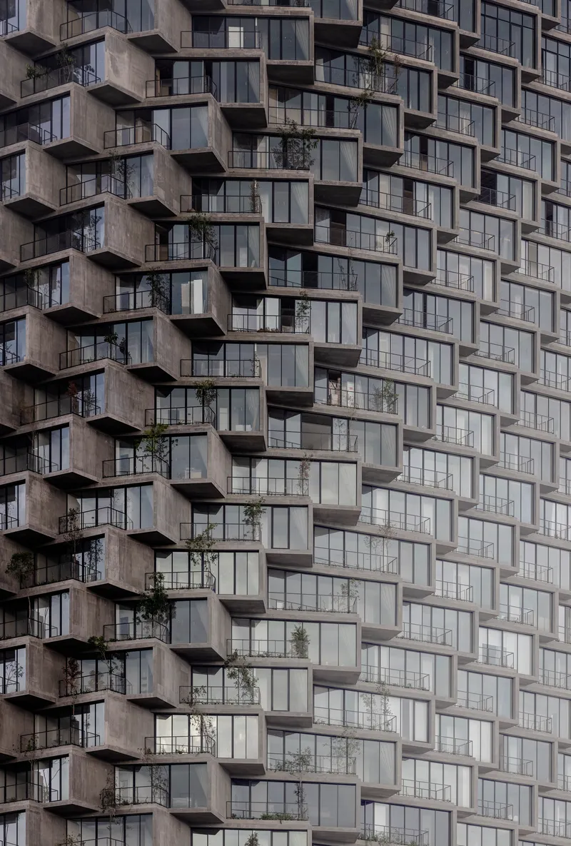 Repetitive concrete balcony grid with recessed glass panels and scattered vegetation