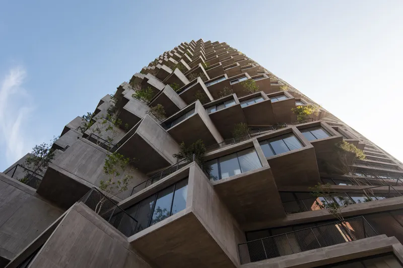 Worm's-eye view of the stacked concrete balconies with planted terraces ascending toward cloudy sky