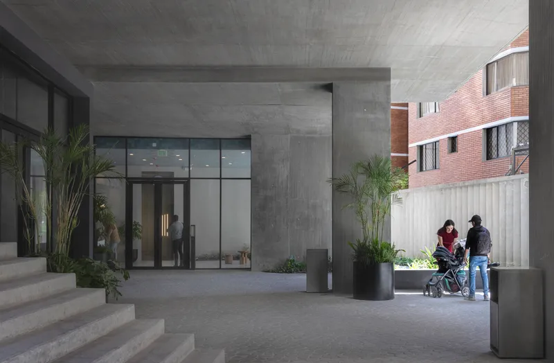 Covered entry courtyard with board-formed concrete ceiling and family with stroller walking past potted palms