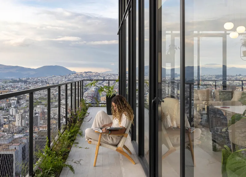 Balcony with metal railing and sliding glass doors overlooking the city at sunset with seated figure