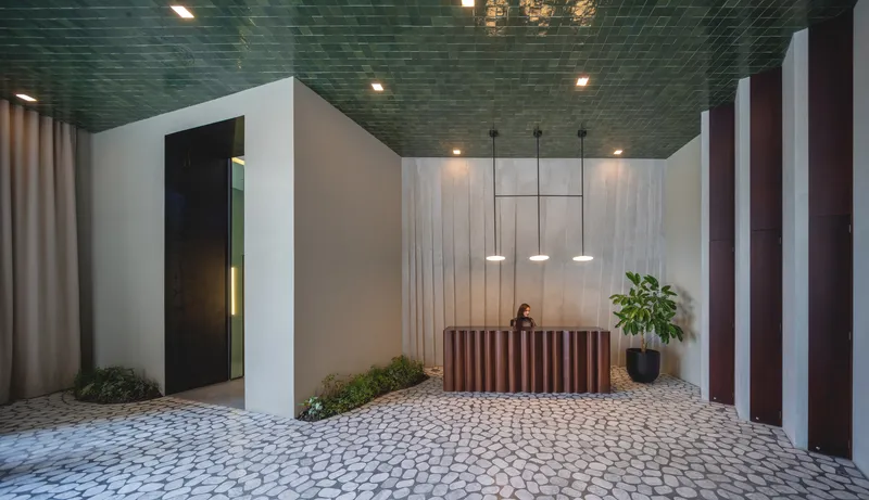 Reception lobby with mosaic stone floor, green glazed tile ceiling and vertical slatted desk with attendant
