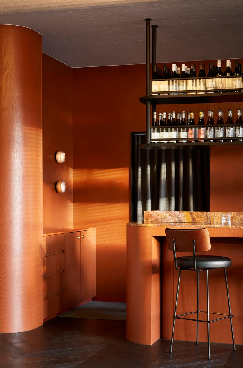 Curved copper-clad column beside bar counter with illuminated shelving and dark stovepipe vent