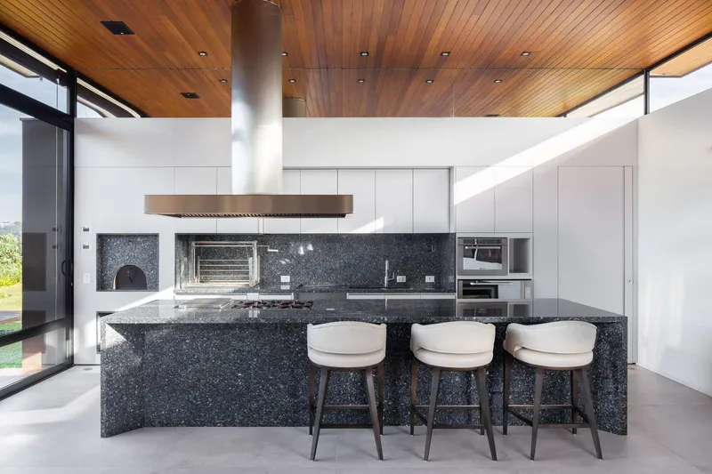 Close view of the black terrazzo kitchen island with three stools under a timber ceiling