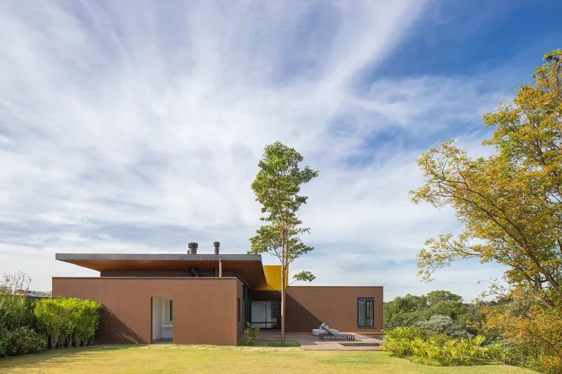 Rear garden view of the flat-roofed volumes with terracotta walls and trees on lawn