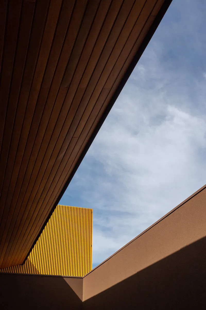 Looking up at the wood soffit framing the yellow perforated screen against blue sky