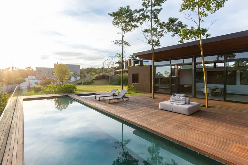 Timber deck terrace with pool and glass pavilion flanked by young trees in late afternoon light