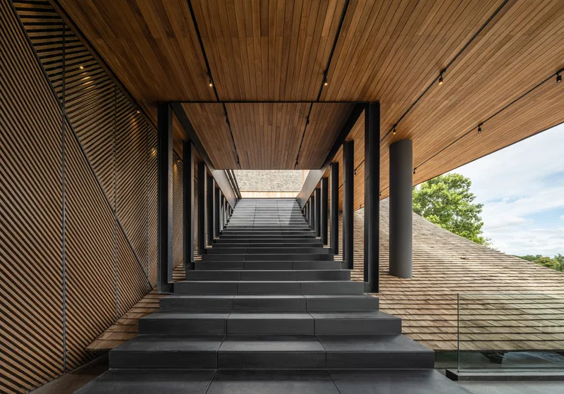 Monumental staircase framed by black structural portals and timber ceiling ascending toward an open courtyard