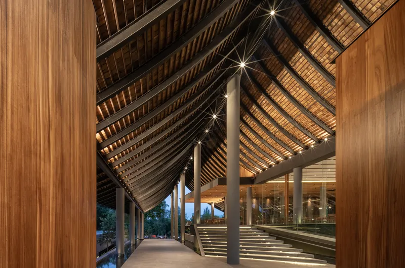 Interior corridor beneath the peaked timber ceiling with layered rafter structure at twilight