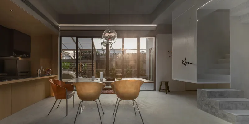 Dining table with copper-toned chairs facing sliding glass doors opening to a timber-screened courtyard at dusk