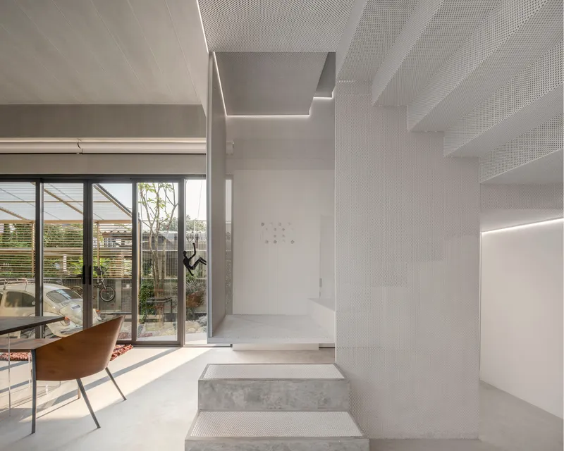 Perforated metal staircase with integrated lighting rising alongside a glazed courtyard view