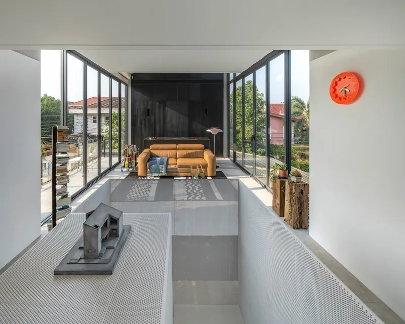 Double-height living space with floor-to-ceiling steel glazing opening to a wooden deck and green treetops