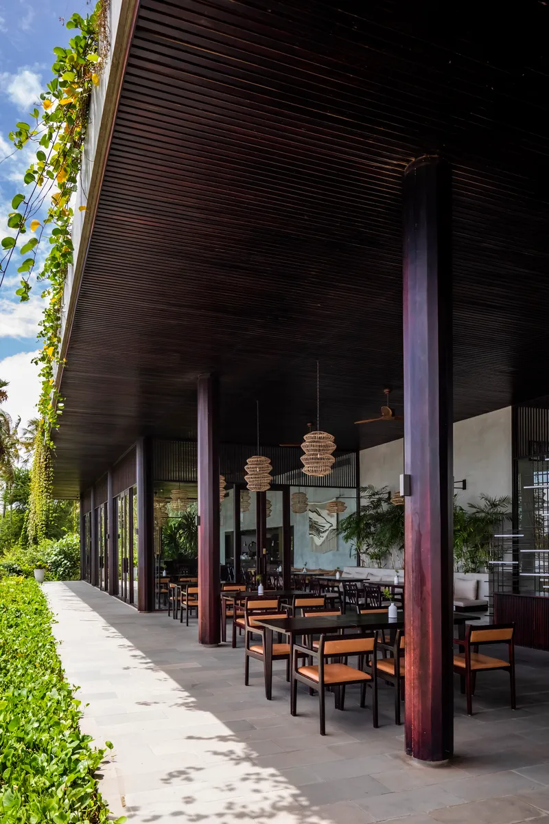 Covered terrace with dark slatted ceiling and steel columns sheltering outdoor dining tables
