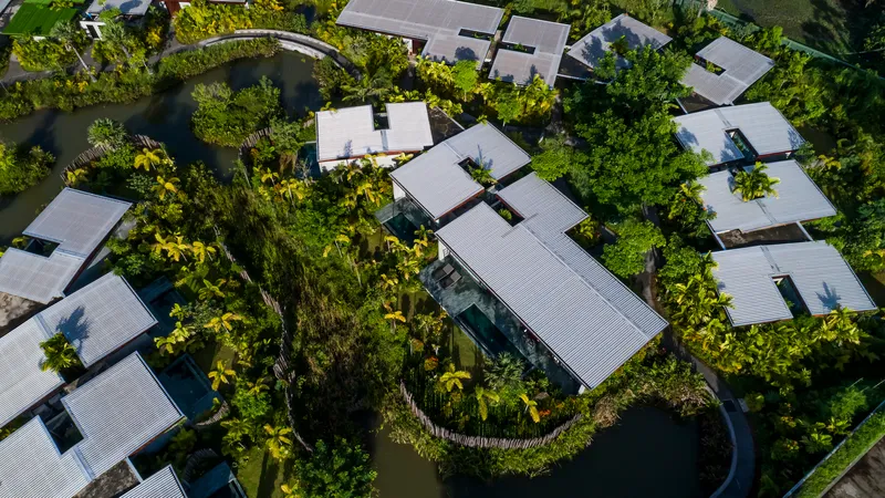 Drone view of corrugated metal roofs arranged among trees and reflecting ponds in a compound