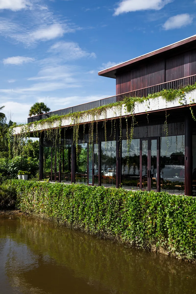 Glass-walled facade with cascading vines along the pergola trellis above a still pond