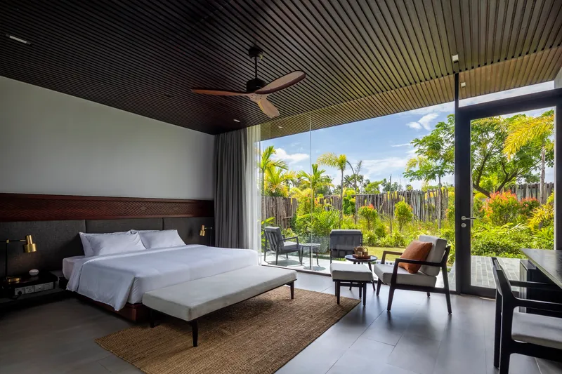 Bedroom with floor-to-ceiling glass doors opening to a garden terrace with tropical plantings