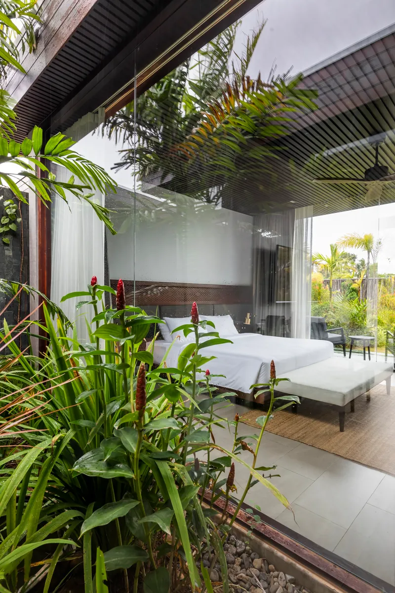 Exterior view of bedroom through planted courtyard with red flowering ginger in foreground
