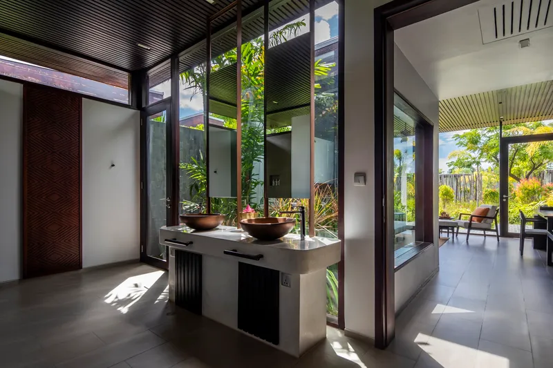 Bathroom with copper vessel sinks on floating vanity flanked by glazed courtyards with tropical plants