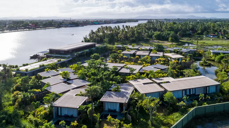 Aerial view of clustered pavilion roofs set among landscaped gardens and water ponds beside a river