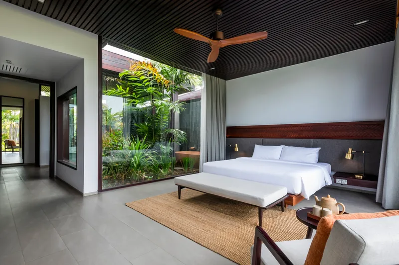 Bedroom interior with slatted black ceiling and full-height glazing opening to a planted courtyard
