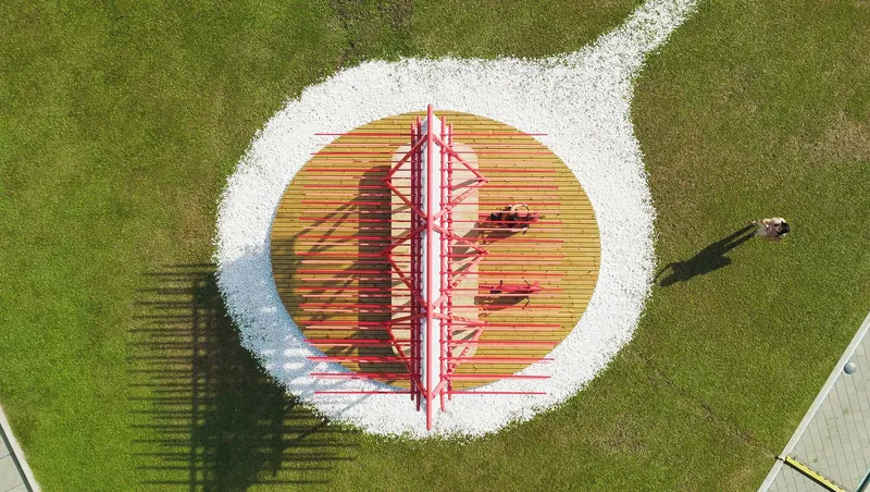 Aerial view of the pavilion on a circular timber deck with white gravel border and a lone pedestrian