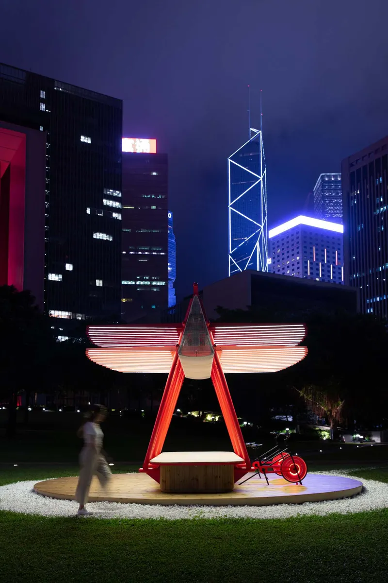 Night view of the illuminated pavilion with horizontal light strips and a blurred figure passing by