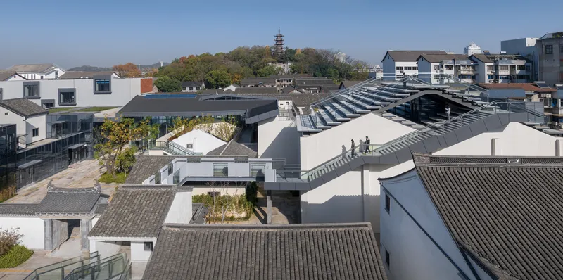 Aerial view of interconnected courtyards with white volumes and grey-tiled roofs among surrounding neighborhood buildings
