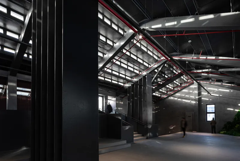 Interior hall with exposed red truss structure and visitors moving through pools of natural light