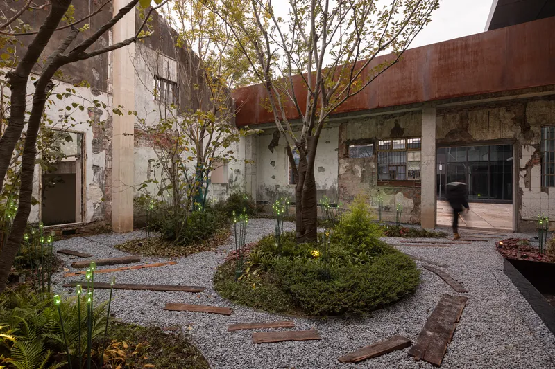 Gravel courtyard with circular planted beds and deciduous trees among weathered concrete walls