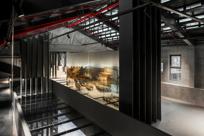 Interior walkway overlooking a central void with landscape display behind glass and vertical black baffles