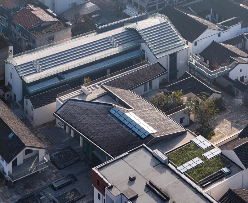 Drone view of the complex showing corrugated metal roofs, skylights, and rooftop gardens among grey tile rooftops