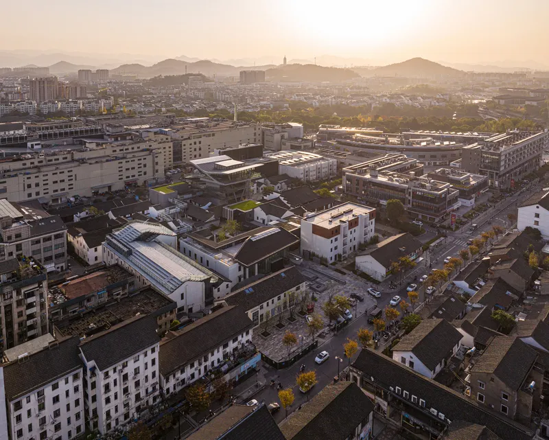 Elevated view across mixed low-rise rooftops and green courtyards at sunset with distant hills