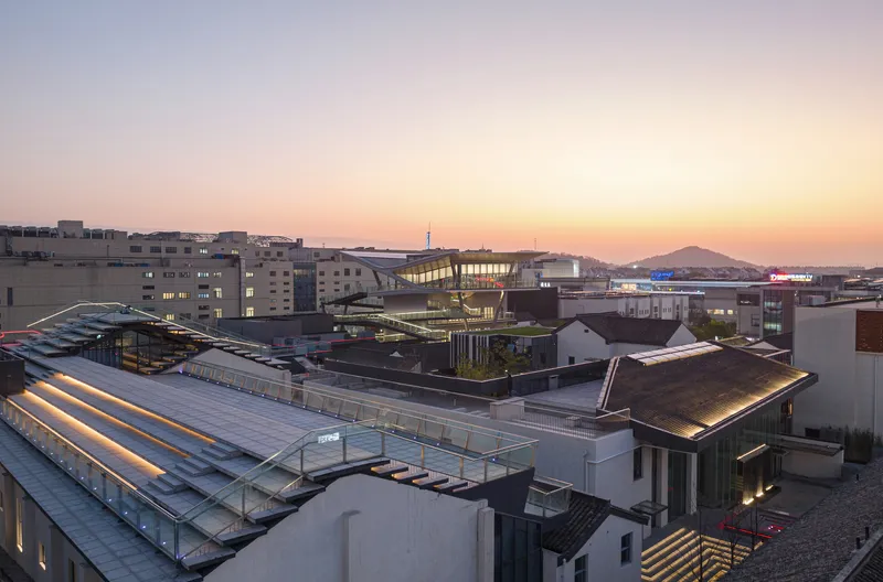 Rooftop cluster with illuminated linear skylight and glass volumes at dusk