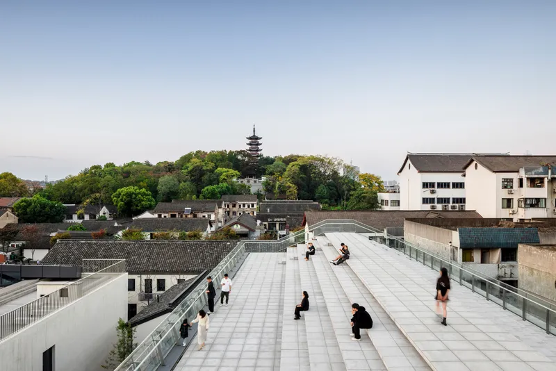 Rooftop terrace with white tile surface and glass balustrades overlooking a pagoda and treetops